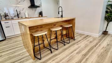 A modern kitchen with a wooden island, bar stools, and a marble backsplash.