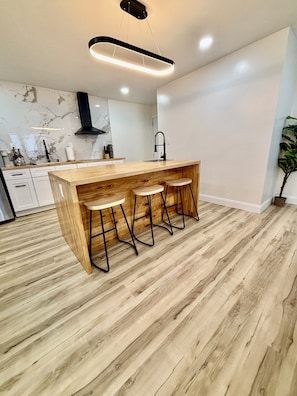 A modern kitchen with a wooden island, bar stools, and a marble backsplash.