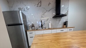 Moderni keittiö, jossa on ruostumattomasta teräksestä valmistettu jääkaappi, puinen työtaso ja marmorista tehty välitilan seinä.