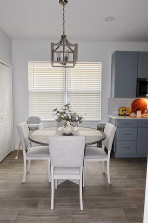 A dining area with a round table, chairs, a vase with flowers, and a hanging light fixture. - Minutes from the Magic .Private Pool • Harry Potter Game Room • Sleeps 10 (Davenport)