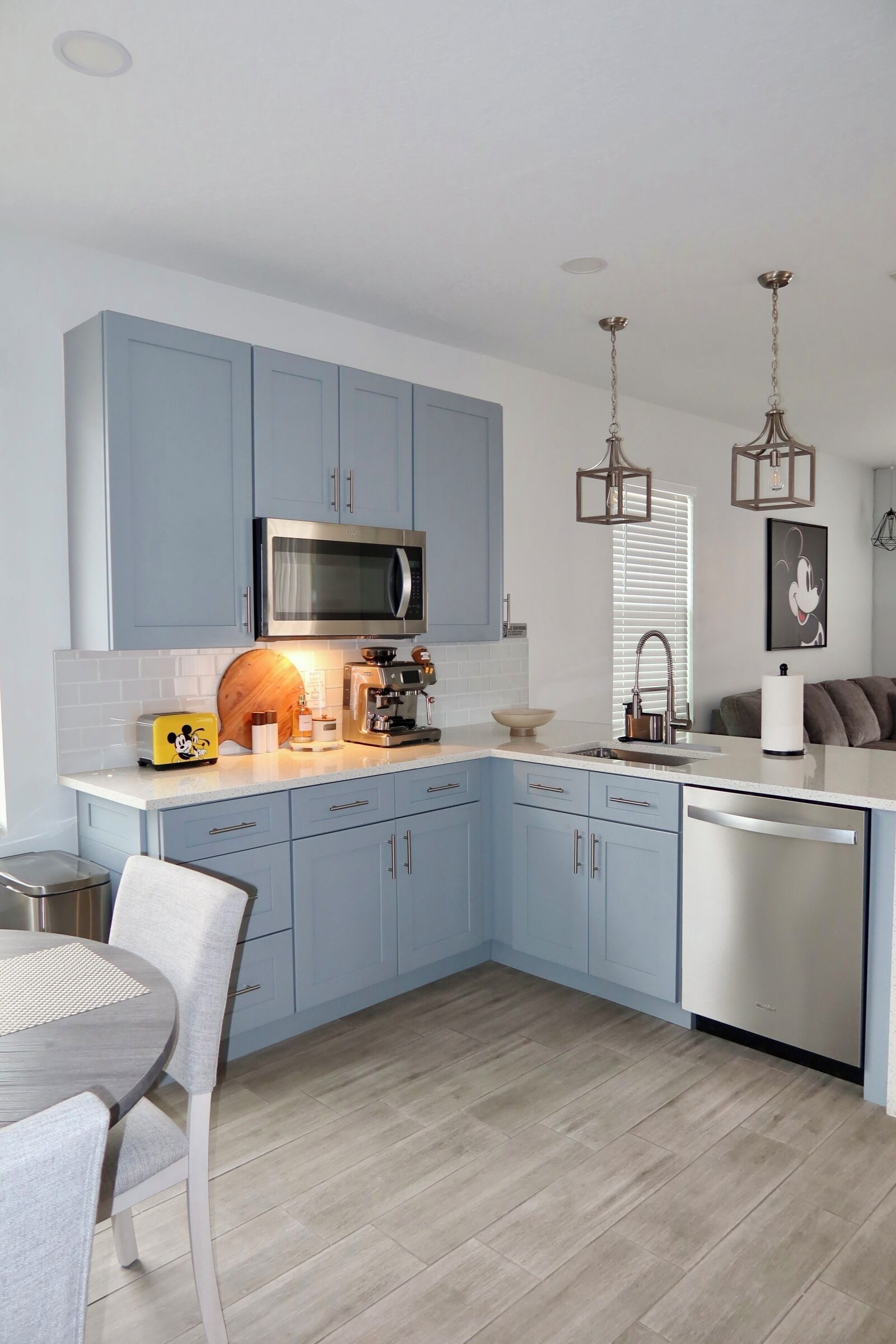 A modern kitchen with blue cabinets, a stainless steel microwave, a coffee machine, and a dishwasher.