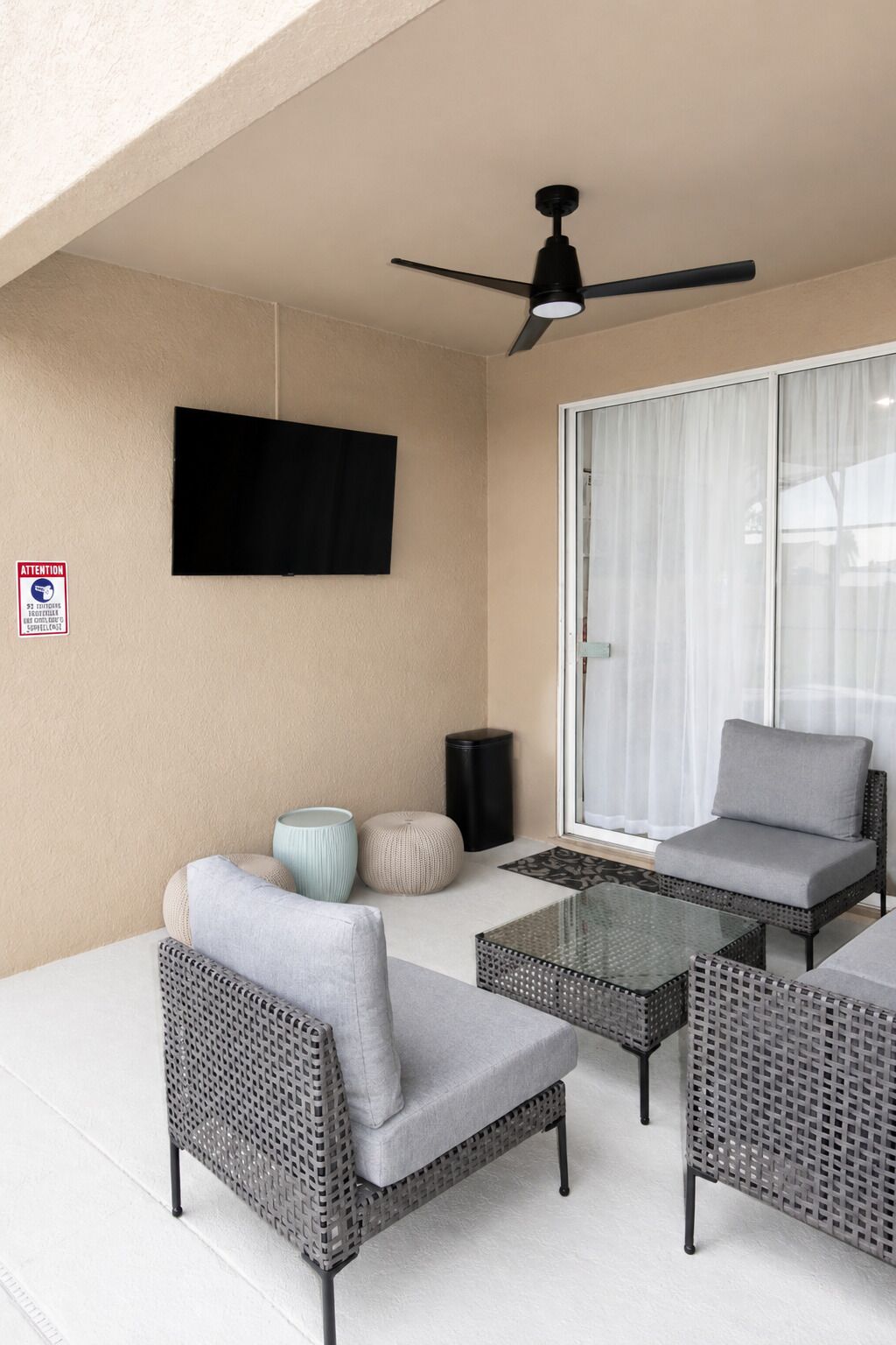 A balcony with wicker furniture, a ceiling fan, a flat-screen TV, and a sliding glass door.