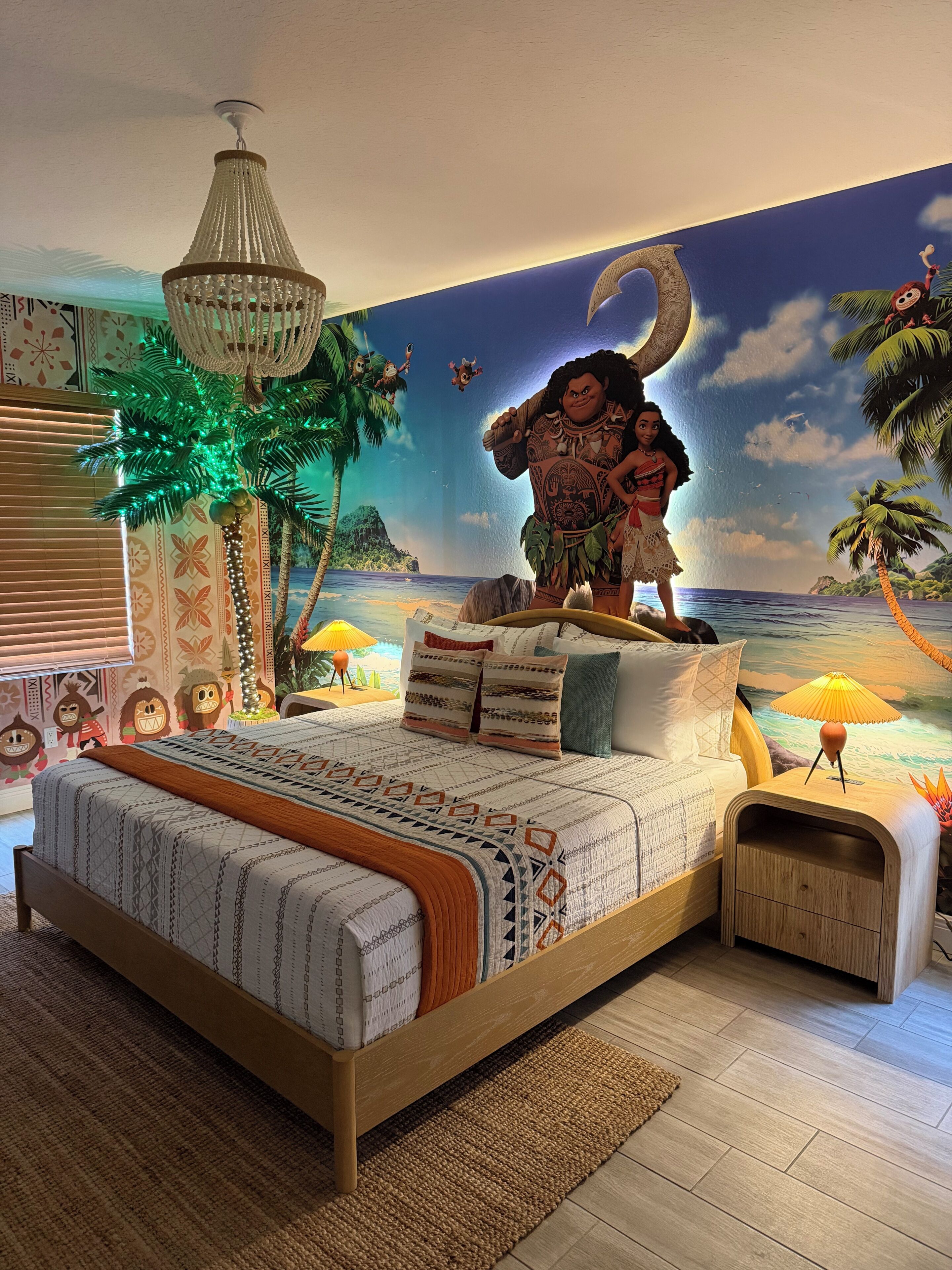 A bedroom with a bed, a nightstand, a lamp, a wall mural, and a ceiling light fixture.