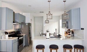 A modern kitchen with stainless steel appliances, a central island with stools, and pendant lighting. - Minutes from the Magic .Private Pool • Harry Potter Game Room • Sleeps 10 (Davenport)