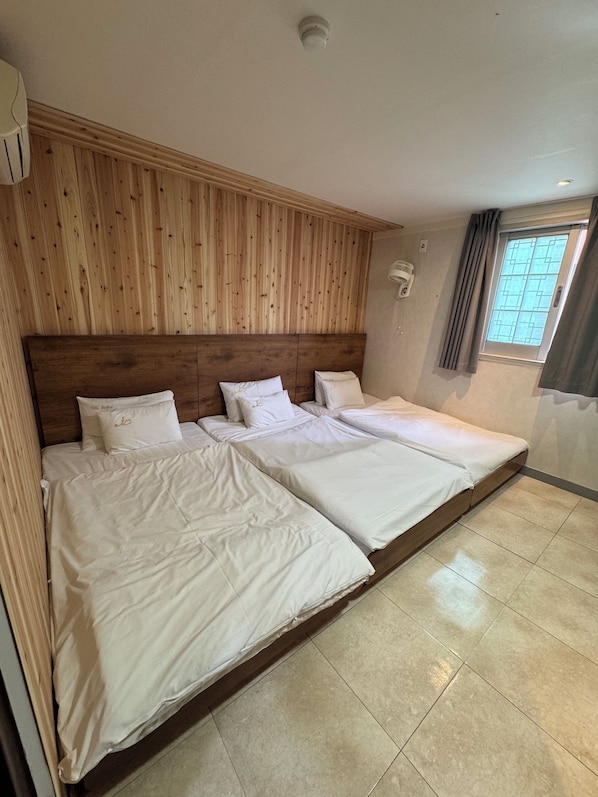 A hotel room with two beds, a wooden headboard, a window with curtains, and a ceiling light.