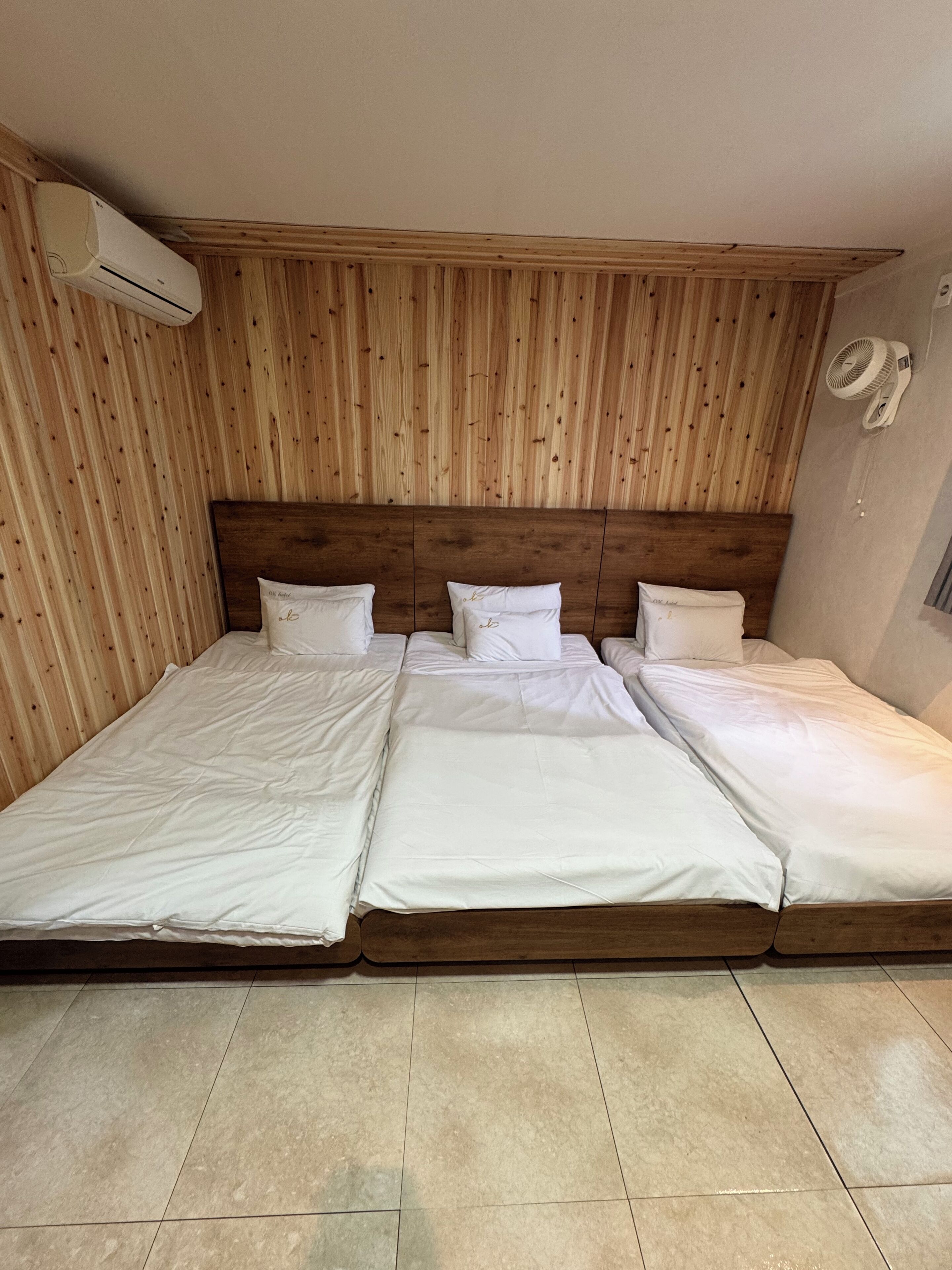 A room with three beds aligned against a wooden wall, each with white bedding and pillows.