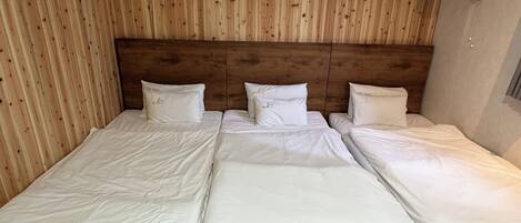 A room with three beds aligned against a wooden wall, each with white bedding and pillows.