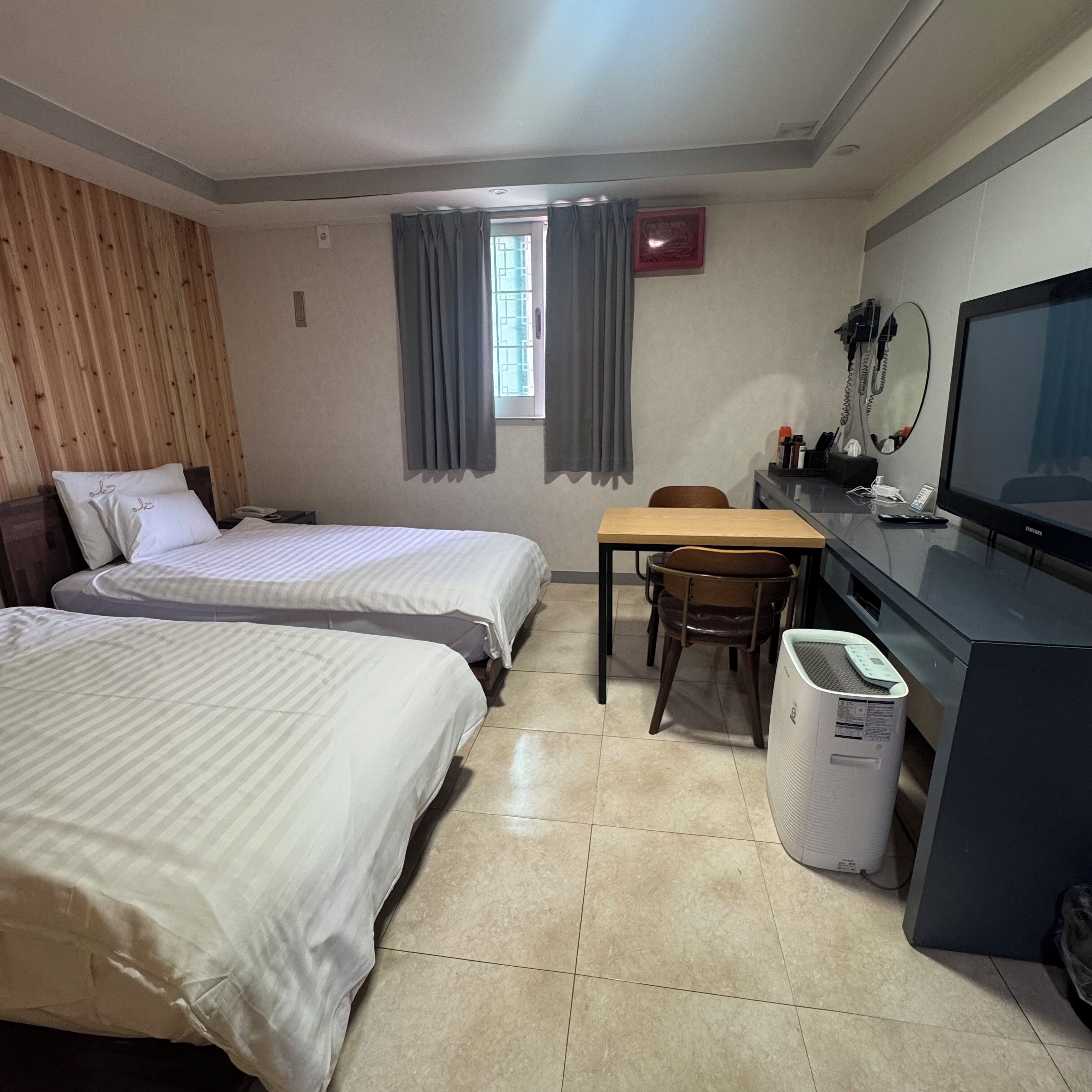 A hotel room with two beds, a desk with a computer, a chair, a television, and a window with curtains.