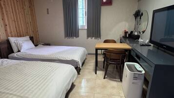 A hotel room with two beds, a desk with a computer, a chair, a television, and a window with curtains.