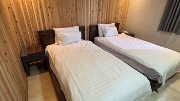 A hotel room with two beds, wooden panel walls, a nightstand with a phone, and a window with curtains.