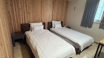Une chambre d’hôtel avec deux lits simples, une tête de lit en bois, une petite table et une fenêtre avec des rideaux.