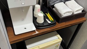 A compact hotel room with a coffee maker, a bag of toiletries, and neatly folded towels on a wooden table.