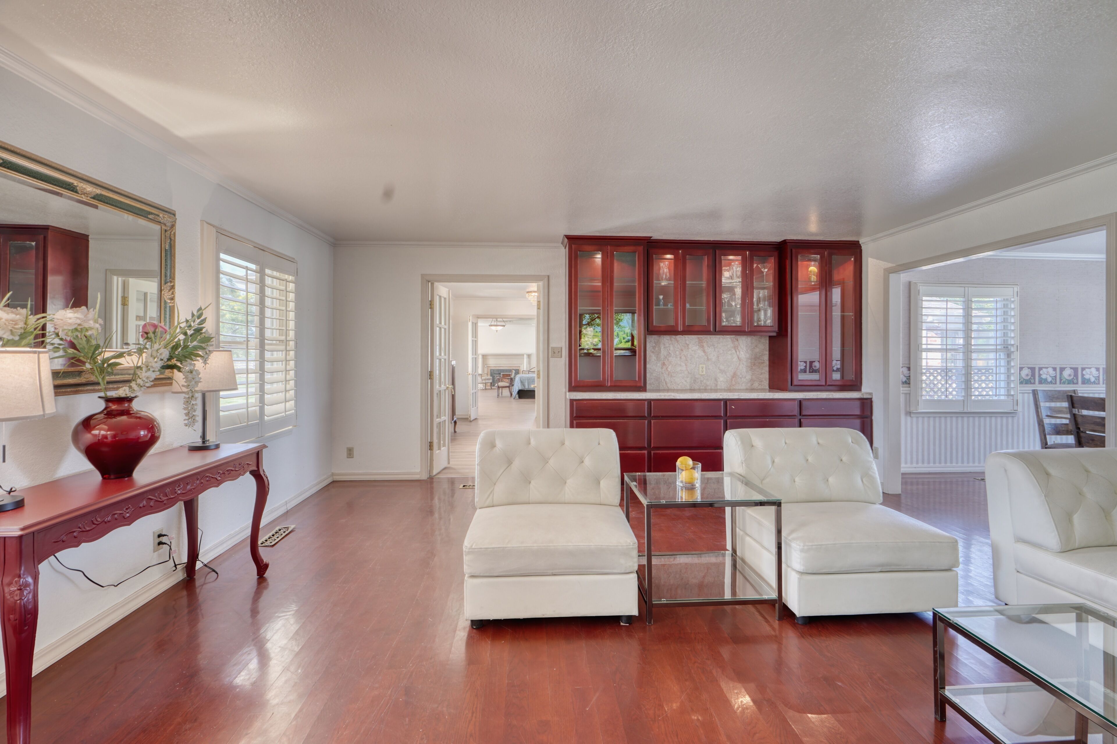 A spacious living room with a wooden floor, a large mirror, and a dining area with a glass table and chairs.