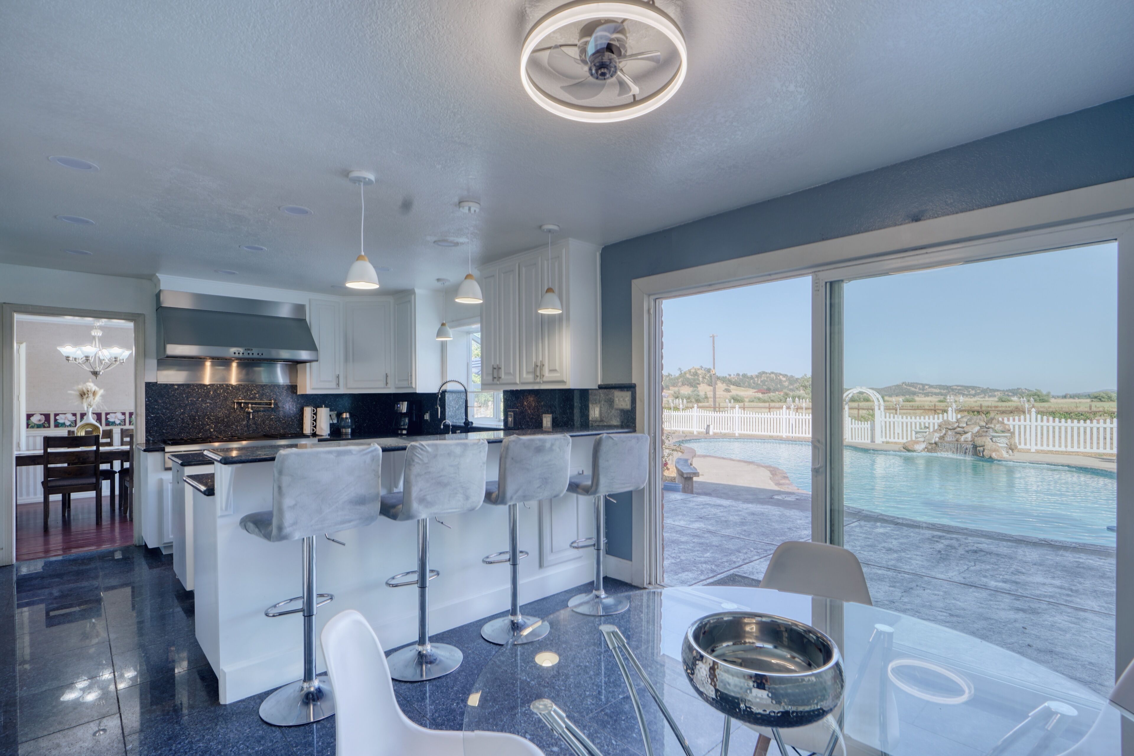A modern kitchen with a central island, bar stools, and a view of a swimming pool.