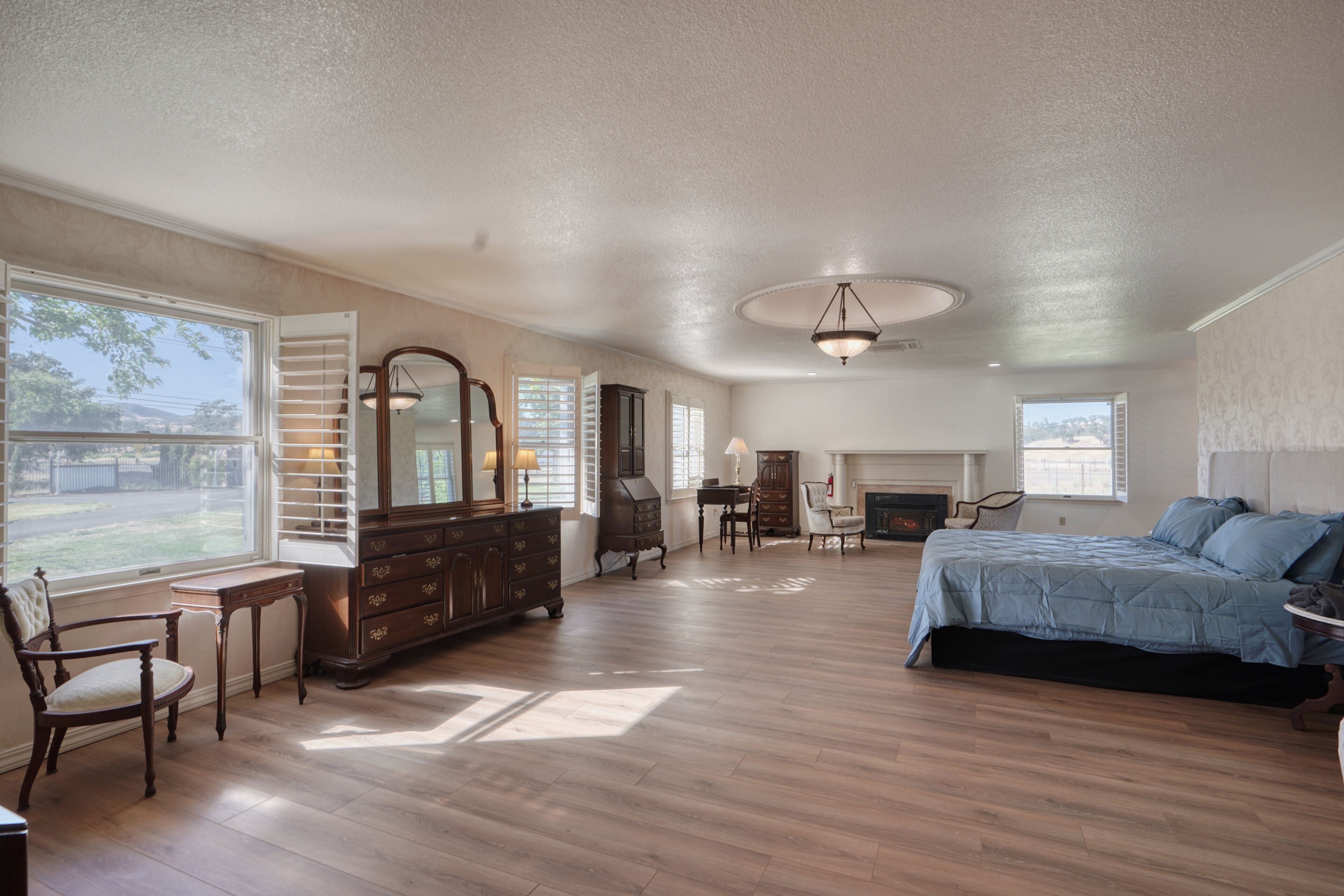 A spacious bedroom with a large bed, a dresser, a chair, and a fireplace.