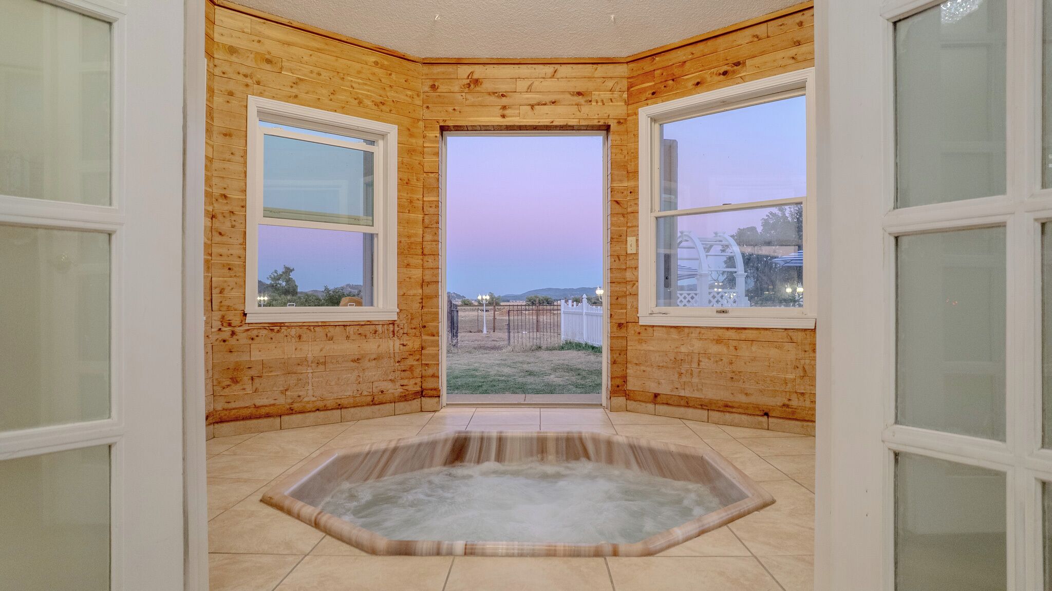 A corner room with wooden walls, two windows, and a hot tub.
