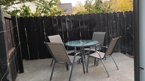 A patio with a round table and four chairs, a wooden fence, and a concrete floor.