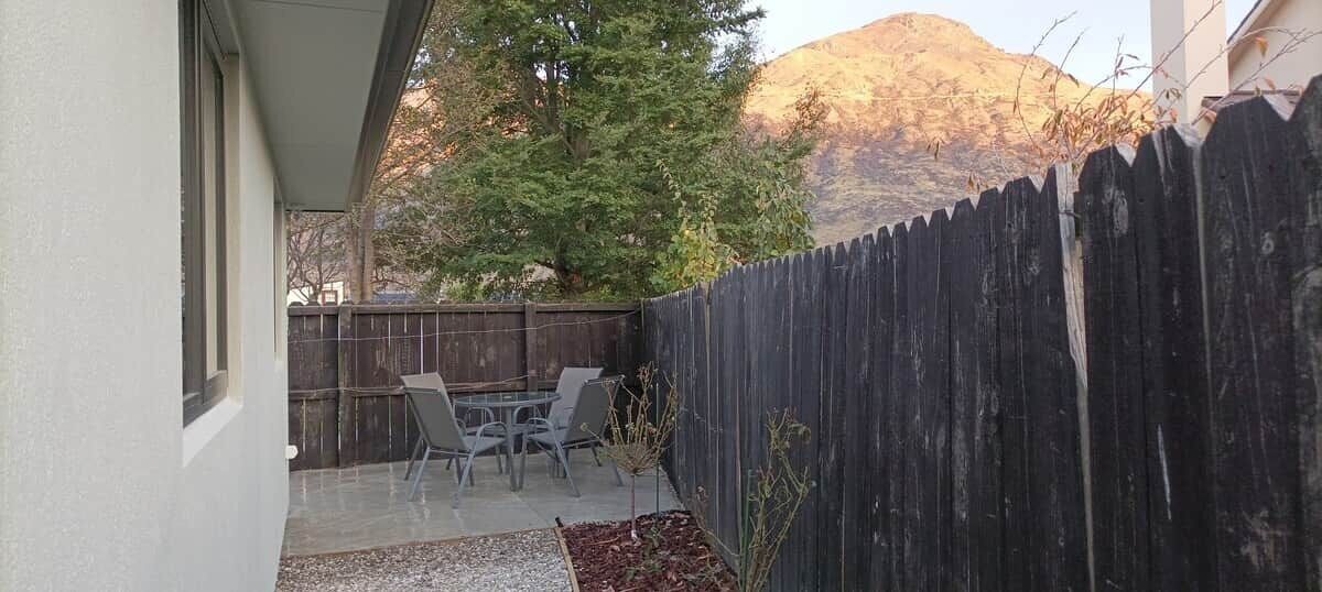 A patio with a table and chairs, a wooden fence, and a mountain in the background.