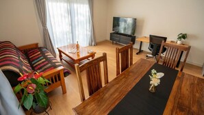 A living room with a sofa, dining table, chairs, a TV, and a small desk with a plant.