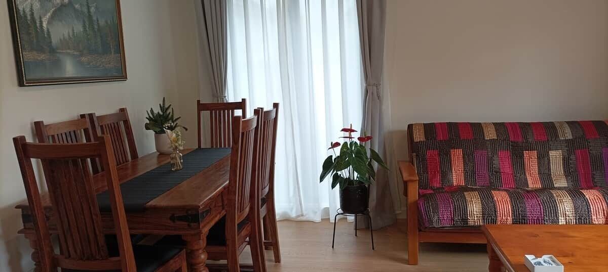 En matplats med ett träbord och stolar, en soffa med ett mönstrat överdrag och en krukväxt.