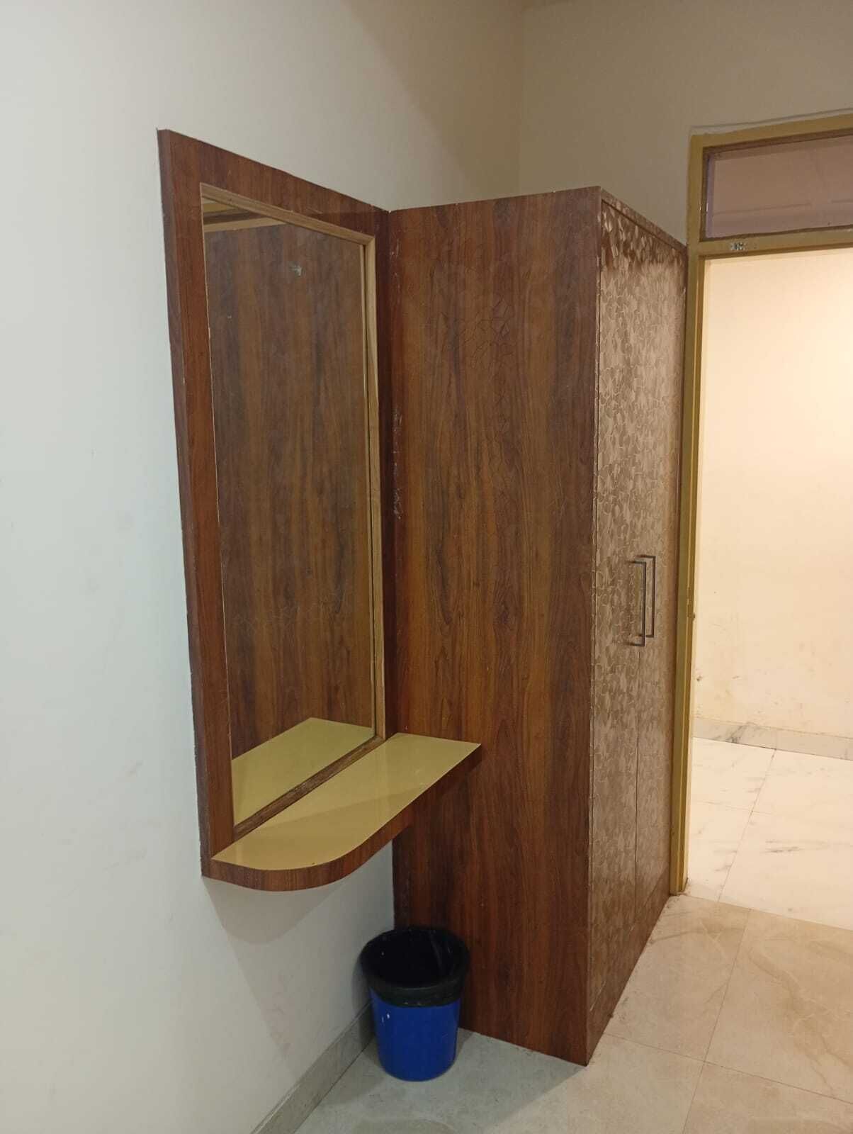 Ein Eckzimmer mit einem Holzschrank, einer kleinen Ablage und einem blauen Mülleimer.