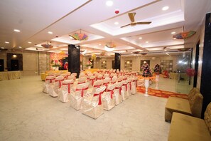 Un salón amplio con filas de sillas, un escenario y elementos decorativos como ventiladores de techo y arreglos florales.