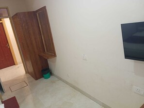 Una habitación con una puerta de madera, un televisor montado en la pared y un bote de basura.