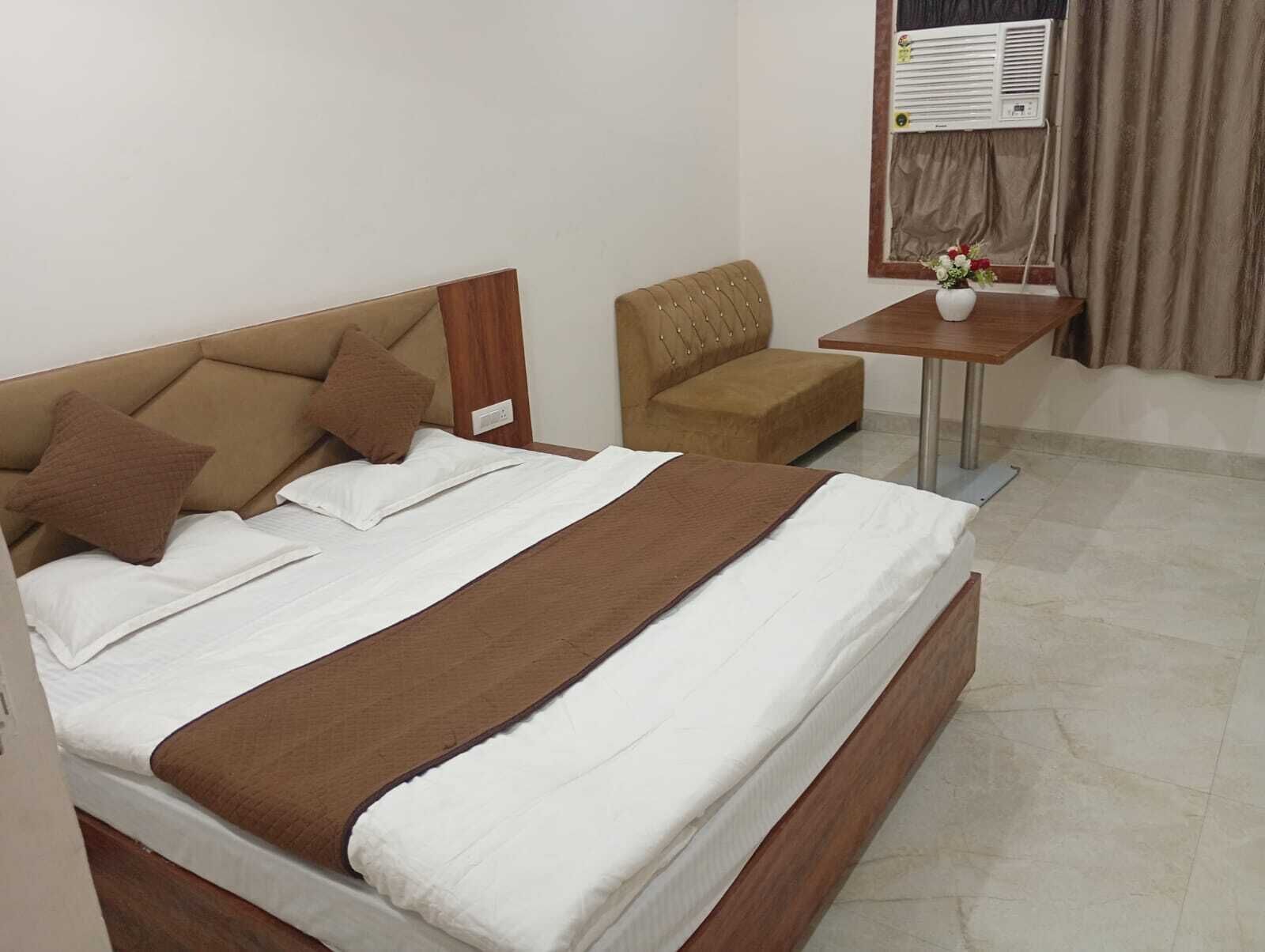 Habitación de hotel con una cama, una silla, una mesita con un florero y un equipo de aire acondicionado en la pared.