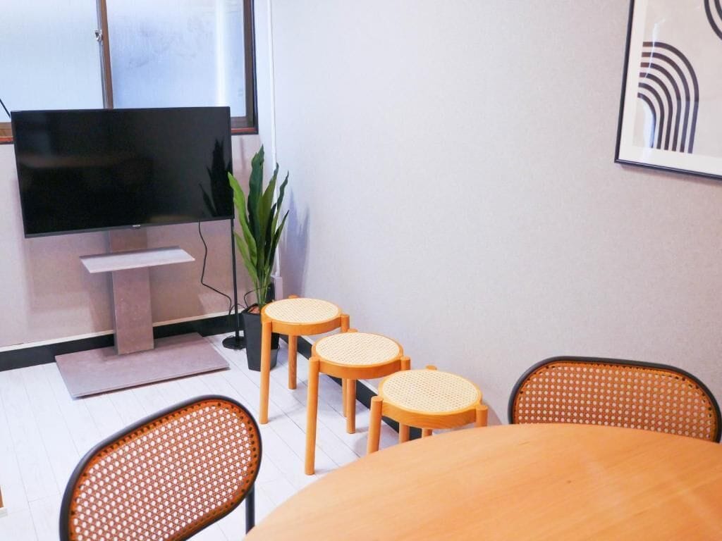 A conference room with a television, a plant, and a round table with four chairs.