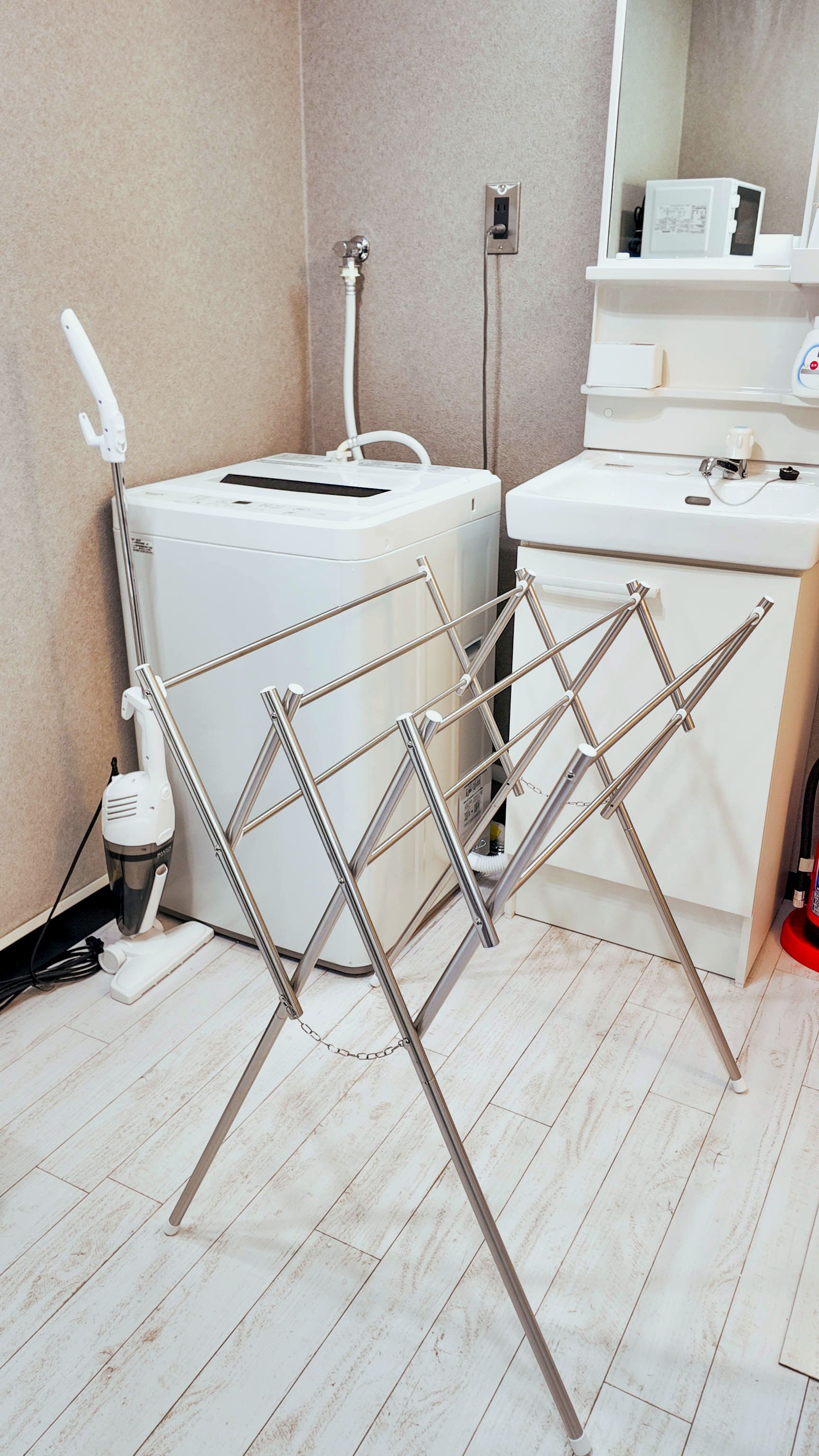 A room with a white washing machine, a drying rack, and a sink with a mirror above it.