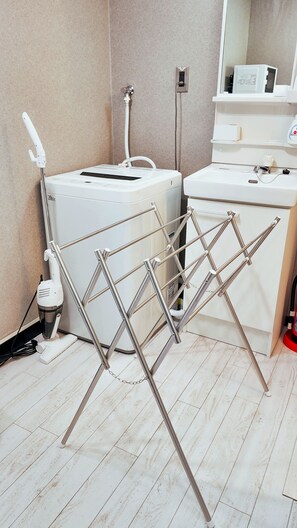 Ein Zimmer mit einer weißen Waschmaschine, einem Wäscheständer und einem Waschbecken mit Spiegel darüber.