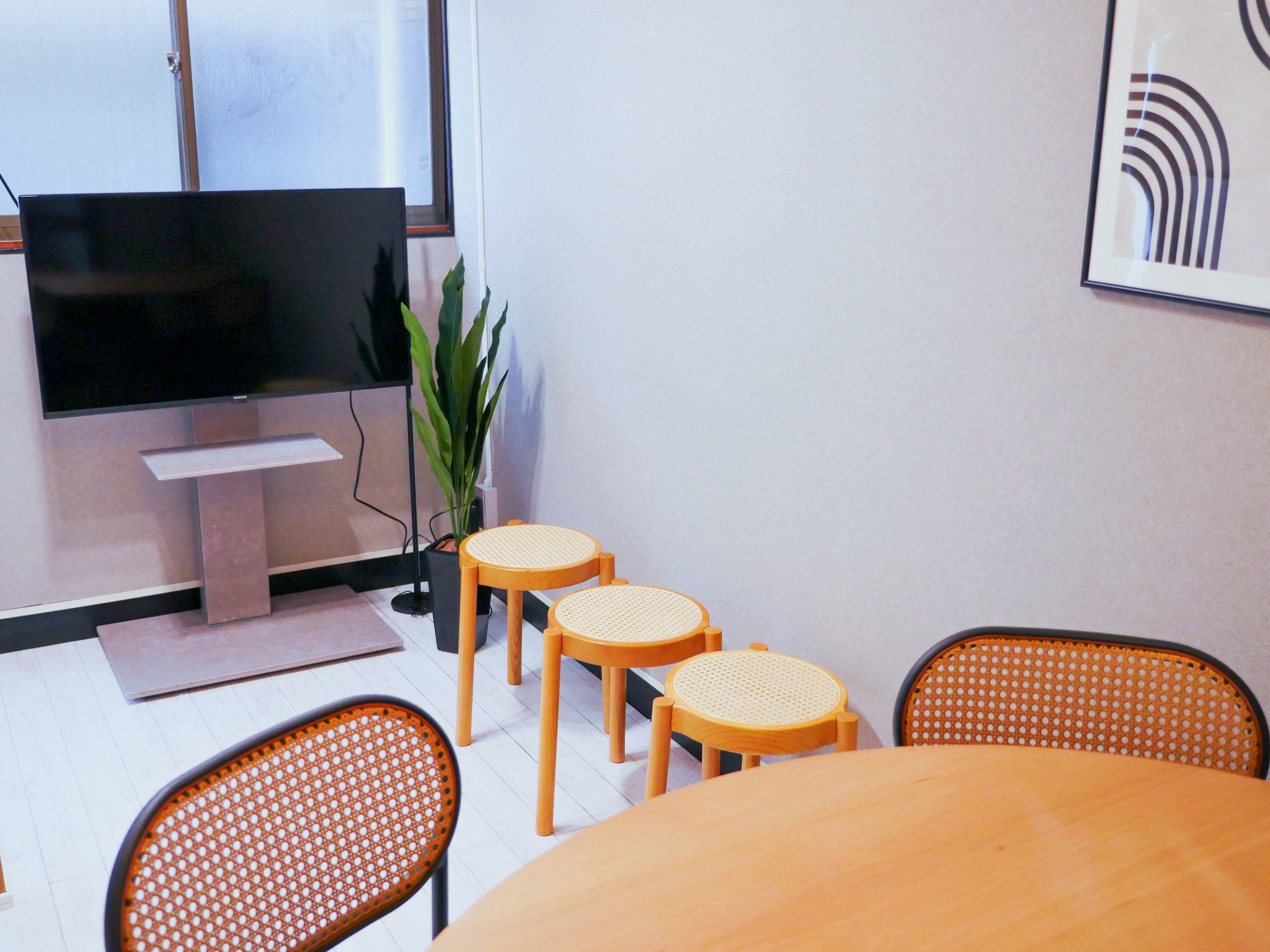 Une salle de conférence équipée d’un grand téléviseur à écran plat, d’une plante en pot et d’une table ronde avec quatre chaises.