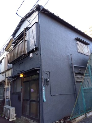 Un edificio residencial con balcón, una puerta con ventana y un cuadro de contadores en la pared.