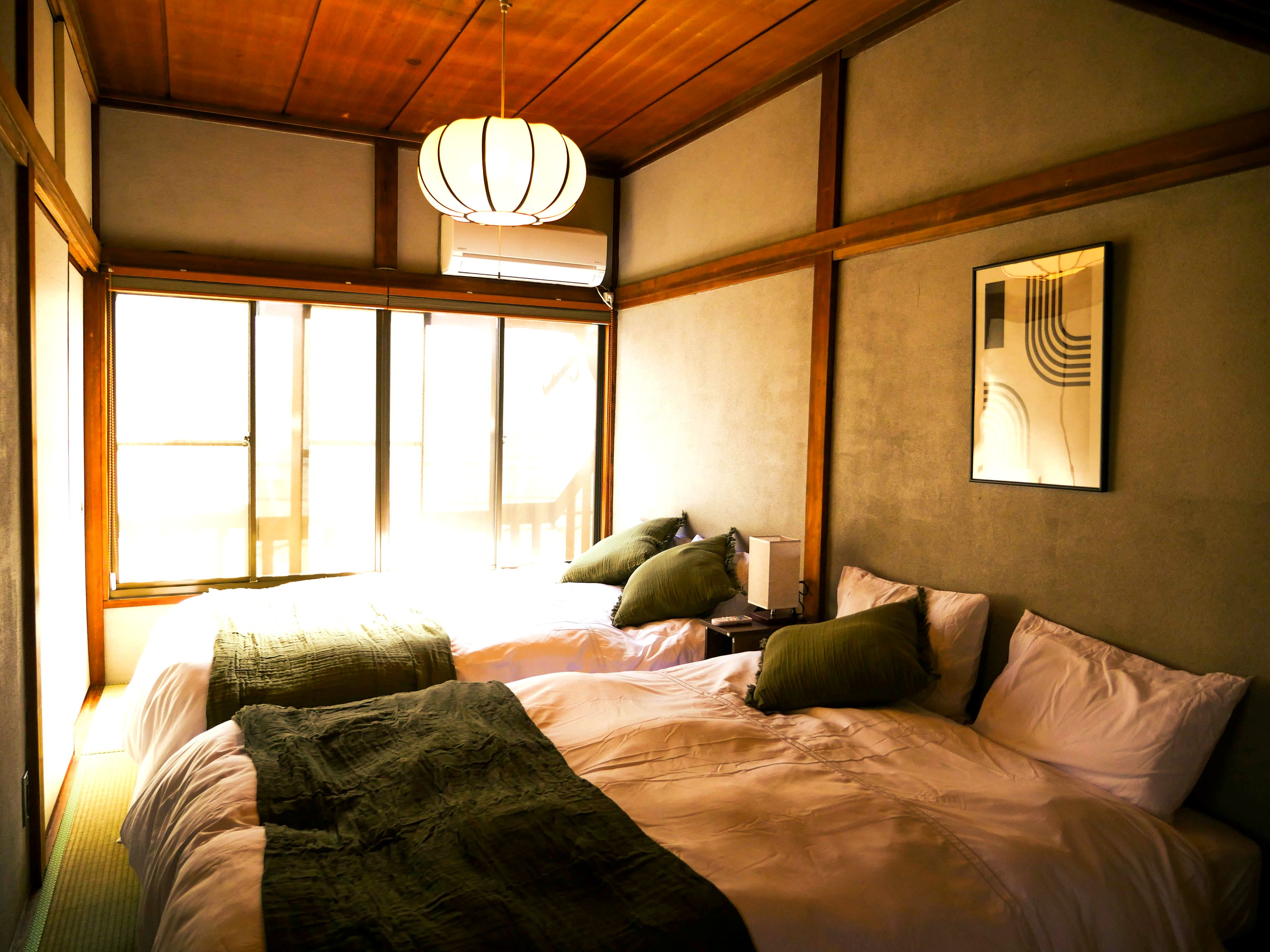 A room with a bed, pillows, a bedside table, a lamp, and a window.
