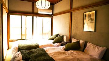 A room with a bed, pillows, a bedside table, a lamp, and a window.