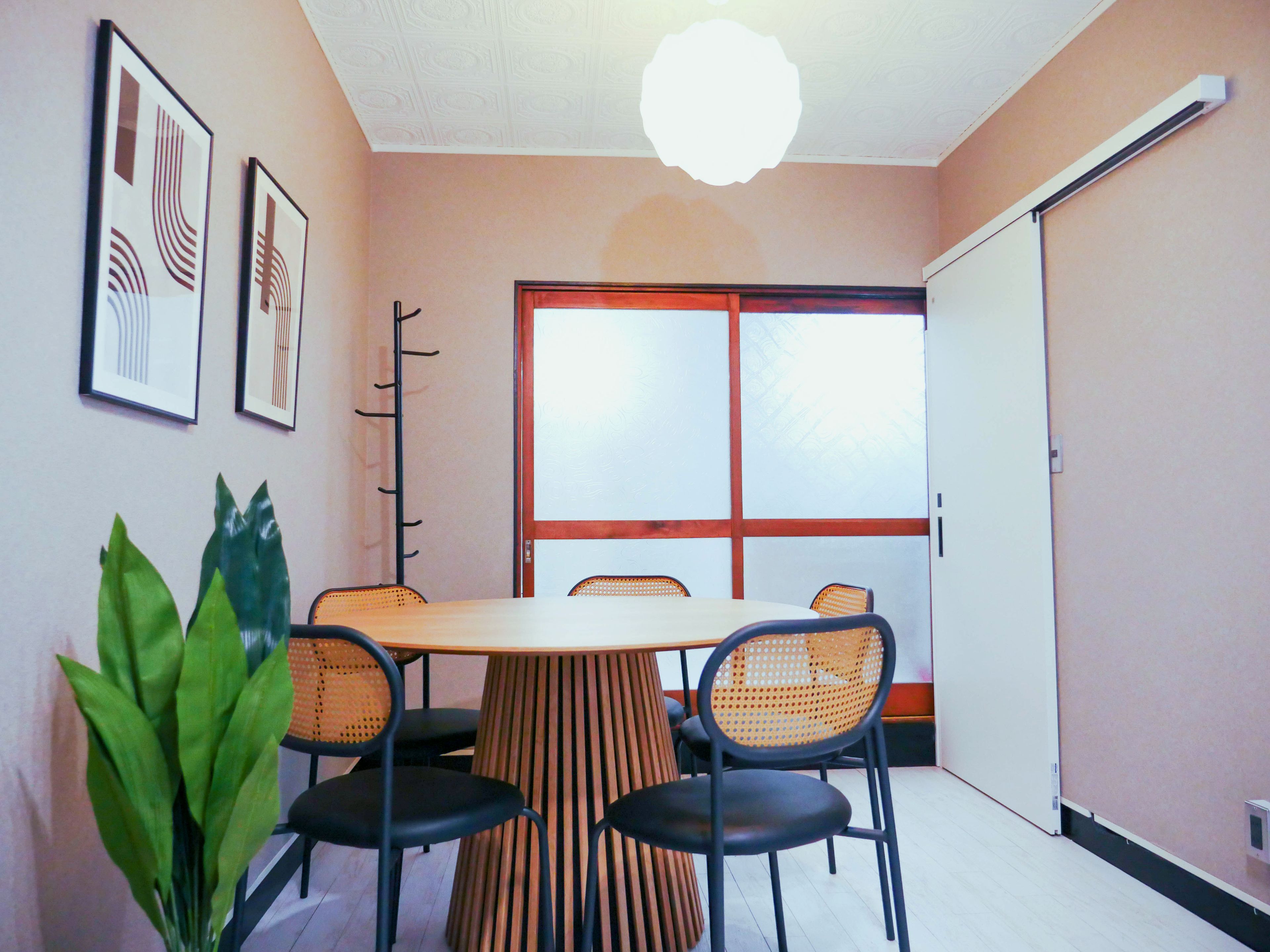 Una habitación con una mesa redonda, cuatro sillas, una planta en maceta y cuadros en la pared.