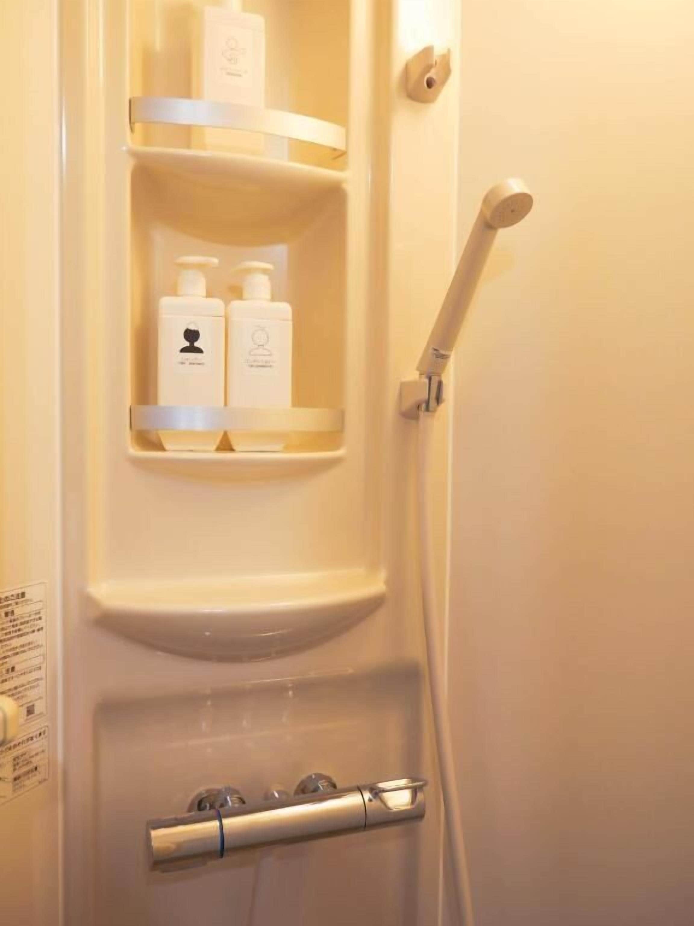A bathroom with a shower, a toilet, and a shelf with toiletries.