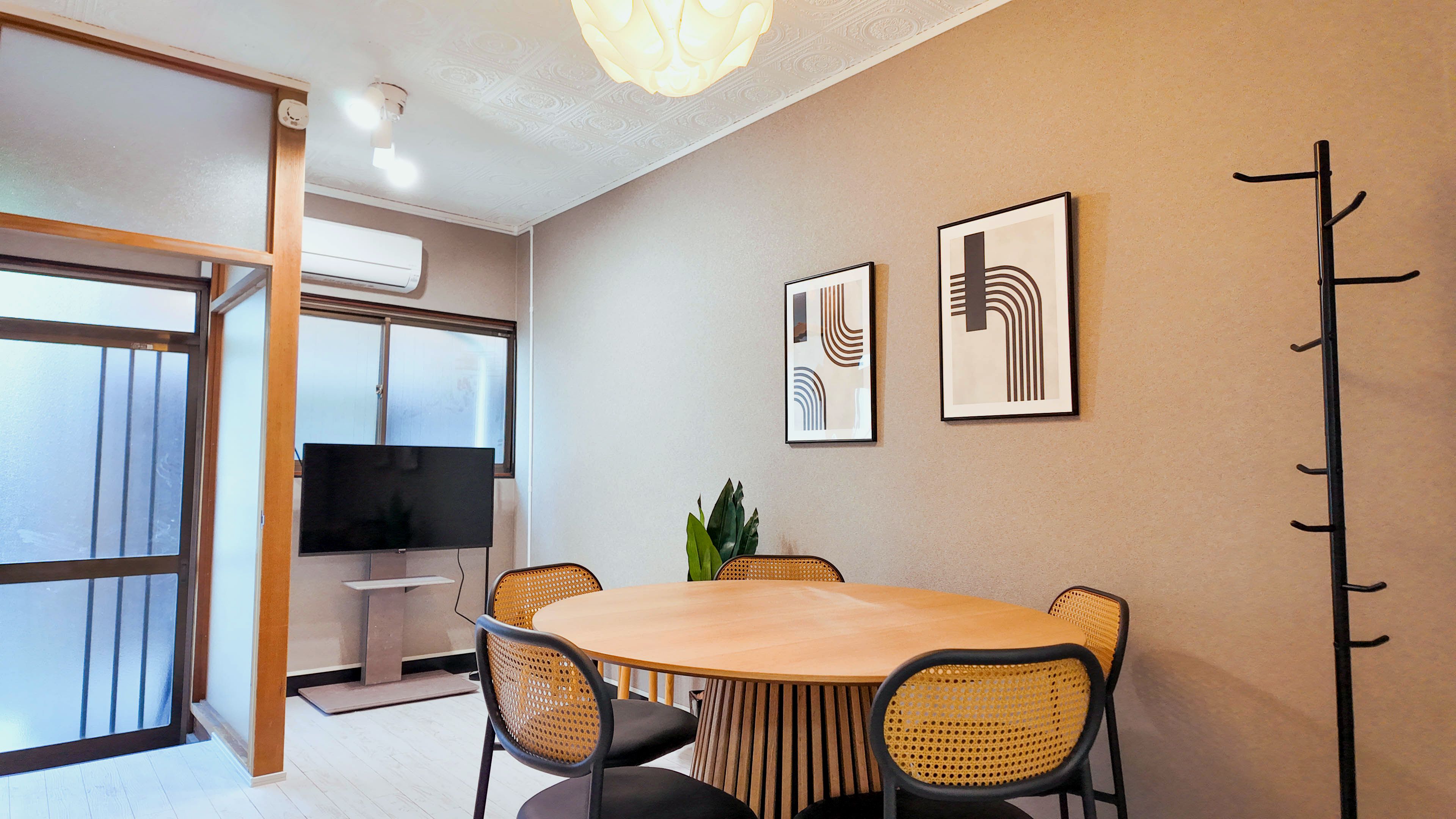A conference room with a round table, four chairs, two framed artworks, a coat rack, and a television.