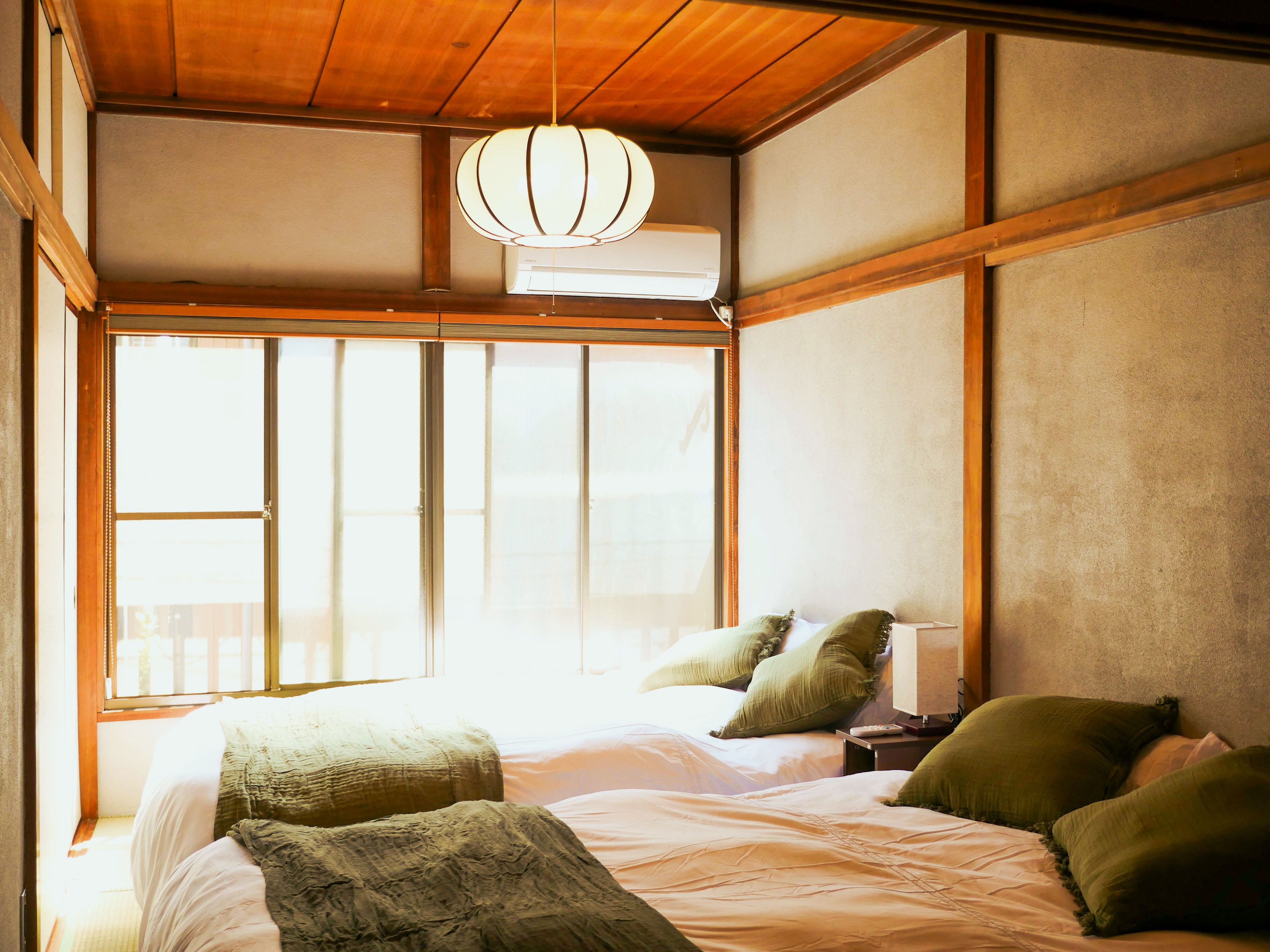 Un dormitorio con un ventanal grande, una cama con muchos almohadones, una mesita de noche y una lámpara colgante.