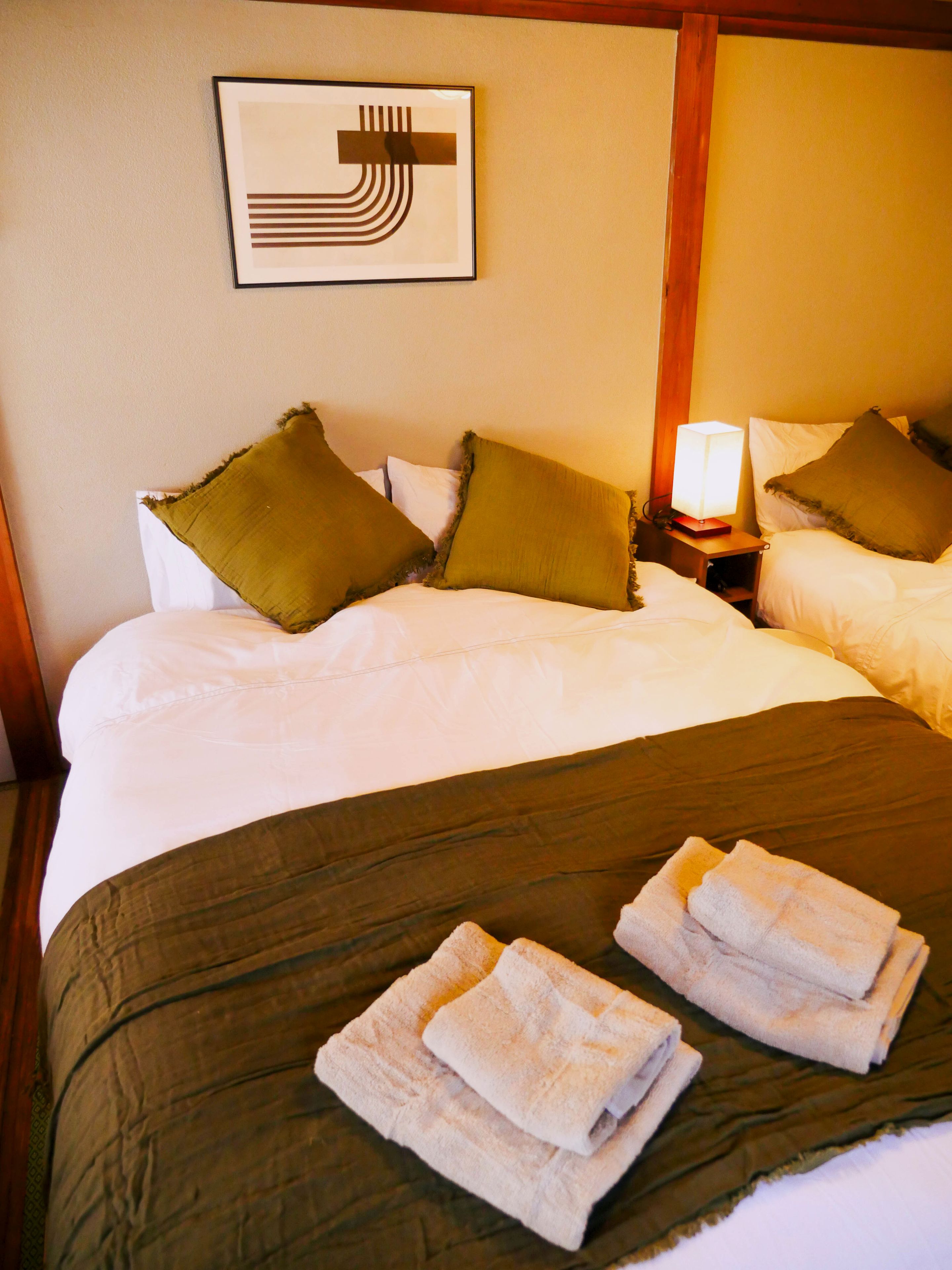 A hotel room with a bed, two pillows, a bedside lamp, and a framed picture on the wall.