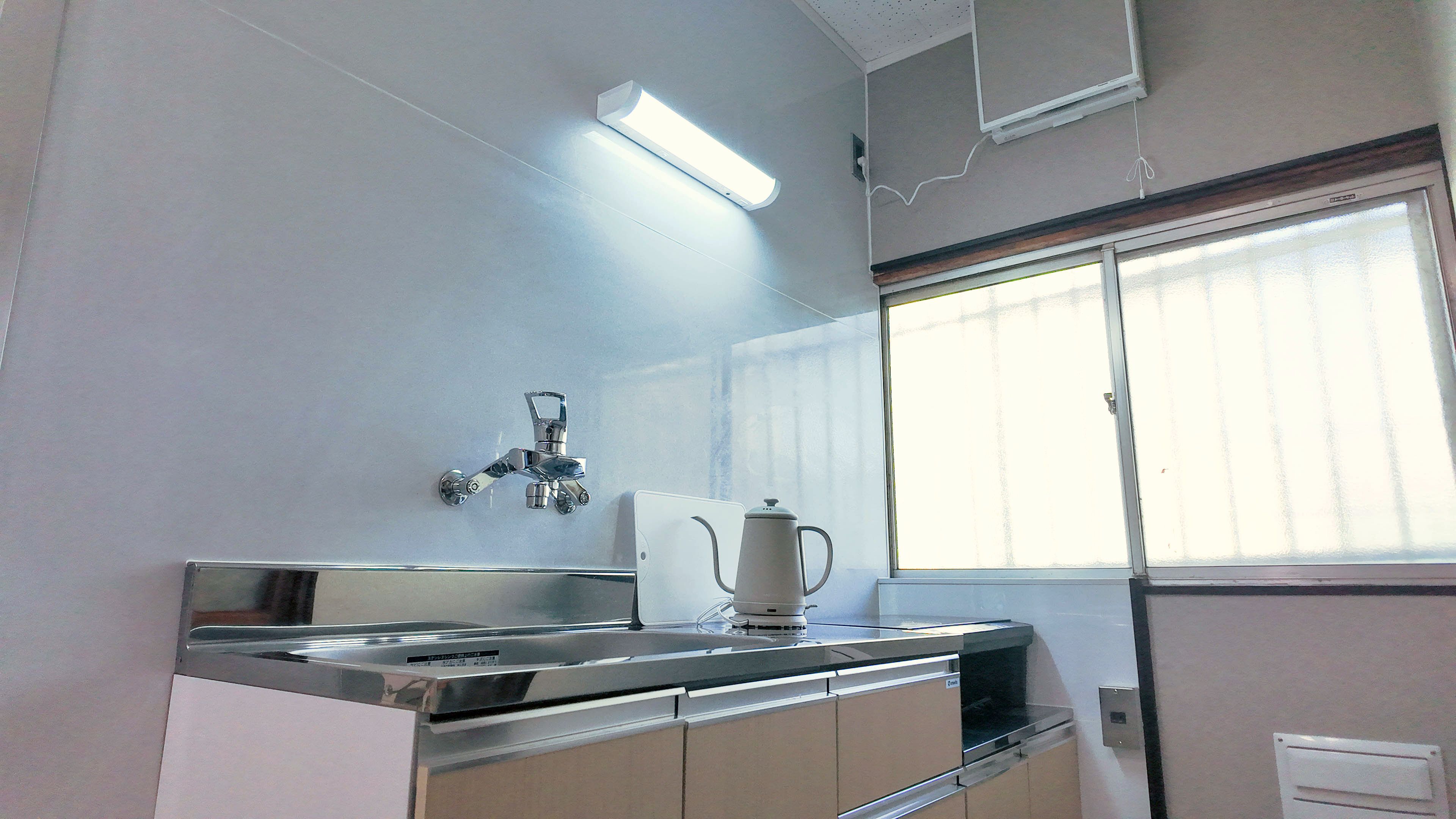 A kitchen with a stainless steel sink, a faucet, a kettle, and cabinets.