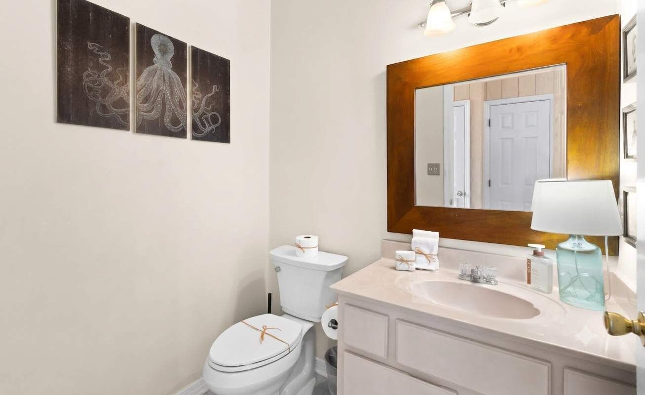 A bathroom with a white toilet, a sink with a mirror above it, and three framed artworks on the wall.