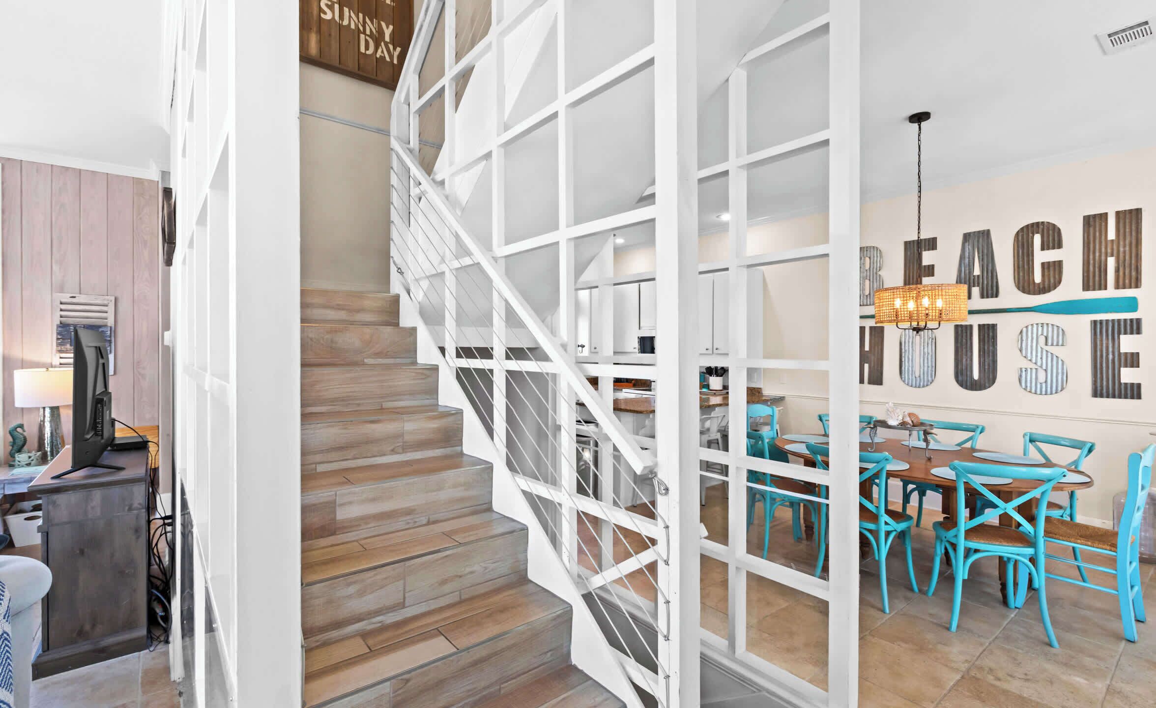 A staircase with a white railing leading to a dining area with turquoise chairs and a chandelier.