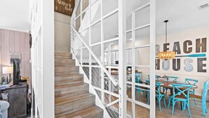 Eine Treppe mit weißer Geländer führt zu einem Essbereich mit türkisfarbenen Stühlen und einem Kronleuchter.