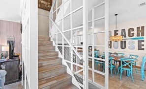 A staircase with a white railing leading to a dining area with turquoise chairs and a chandelier. - My Blue Sky - 4 Bikes, Fire Pit & Porch Paradise (Santa Rosa Beach)