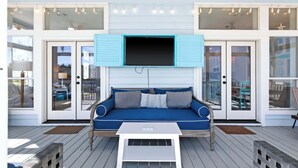 Ein überdachter Außenbereich mit einer blauen Couch, einem darüber montierten Fernseher und einem Holzboden.