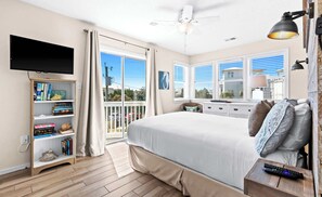 A bedroom with a large bed, a TV, a bookshelf, and a balcony with a view. - My Blue Sky - 4 Bikes, Fire Pit & Porch Paradise (Santa Rosa Beach)