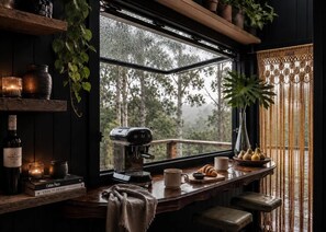 A cozy cabin interior with a coffee machine, books, and a window overlooking a forest.