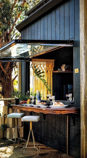 Un espace bar extérieur doté d’un comptoir en bois, de tabourets et d’un auvent.