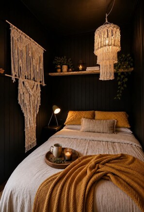 A bedroom with a bed, macramé wall hangings, a hanging light fixture, and a bedside table with a lamp.